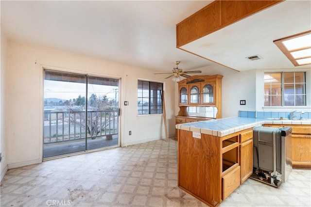 kitchen featuring visible vents, tile counters, brown cabinetry, ceiling fan, and light floors