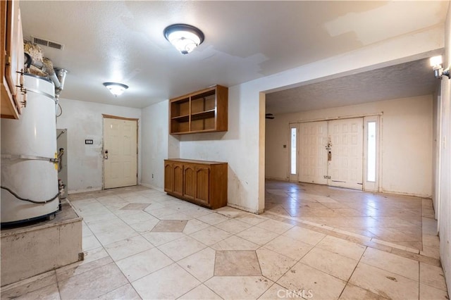 foyer with strapped water heater, visible vents, a textured ceiling, and baseboards