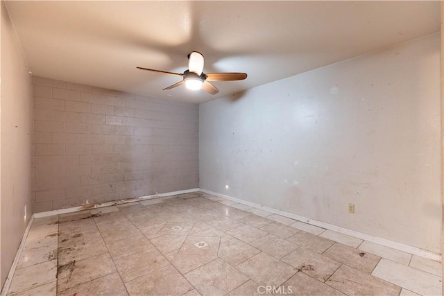 spare room featuring concrete block wall, ceiling fan, and baseboards