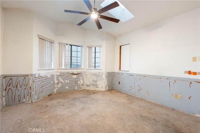 carpeted spare room featuring lofted ceiling with skylight and a ceiling fan