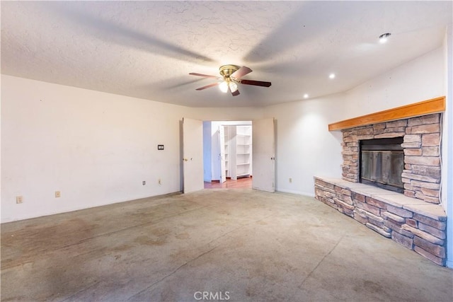 unfurnished living room featuring concrete flooring, ceiling fan, a stone fireplace, and a textured ceiling