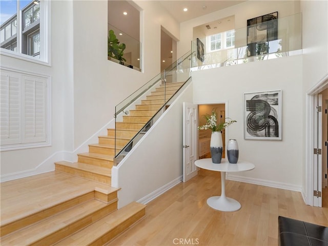 stairs with recessed lighting, baseboards, a high ceiling, and wood finished floors