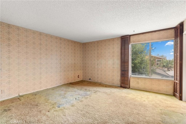 spare room featuring carpet floors, a textured ceiling, and wallpapered walls