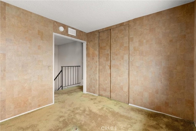 spare room featuring carpet, visible vents, and a textured ceiling