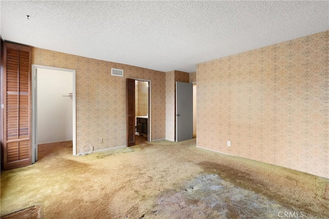 unfurnished bedroom featuring a textured ceiling, carpet flooring, visible vents, and wallpapered walls