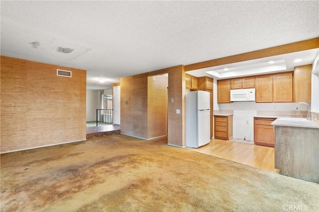 kitchen featuring white appliances, visible vents, light colored carpet, a textured ceiling, and a sink