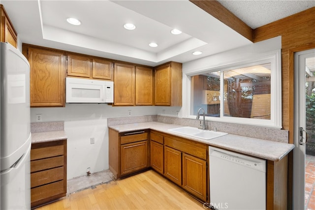 kitchen with a raised ceiling, white appliances, a sink, and brown cabinets