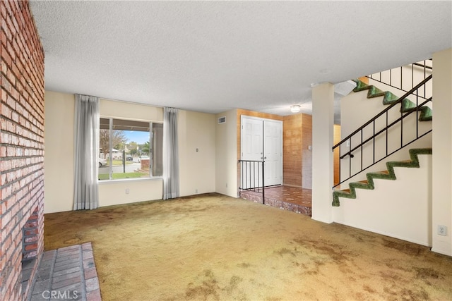 unfurnished living room featuring stairway, visible vents, carpet flooring, and a textured ceiling