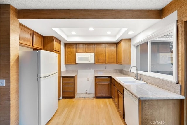 kitchen featuring brown cabinetry, a tray ceiling, white appliances, and a sink