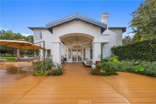 back of property with french doors, a chimney, a wooden deck, and stucco siding