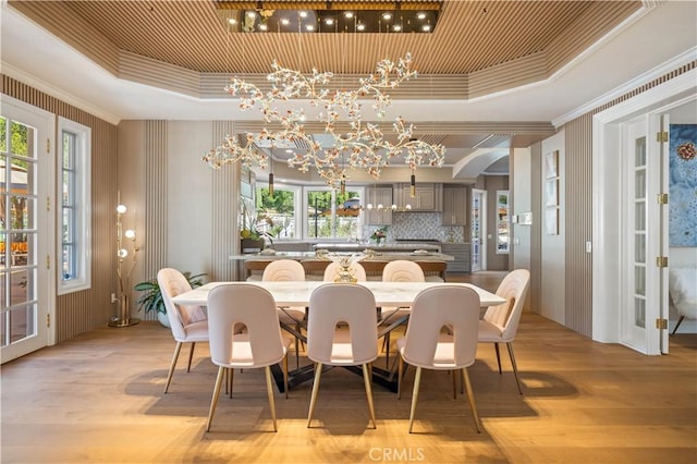 dining space featuring a tray ceiling, arched walkways, crown molding, light wood-style flooring, and a chandelier