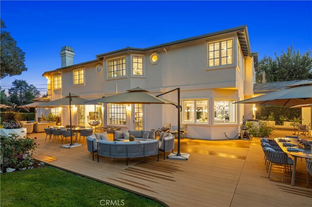 rear view of property featuring a deck, a chimney, outdoor lounge area, and stucco siding