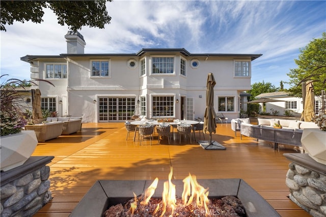 rear view of house featuring an outdoor living space with a fire pit, a wooden deck, and stucco siding