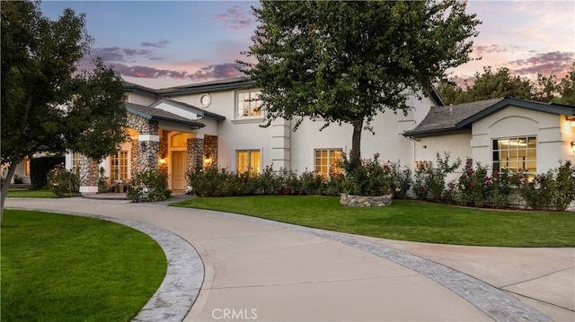 view of front of house with stone siding, a lawn, driveway, and stucco siding