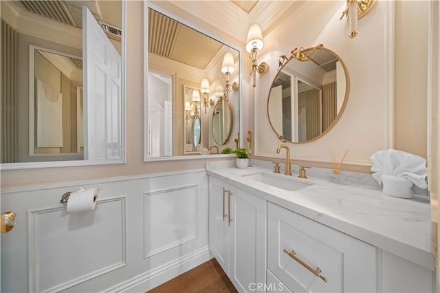 bathroom featuring a wainscoted wall, wood finished floors, crown molding, vanity, and a decorative wall