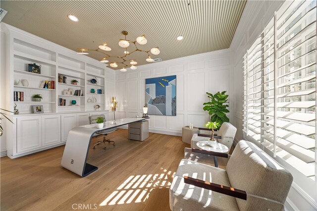 home office with built in shelves, a decorative wall, light wood-style flooring, ornamental molding, and a chandelier