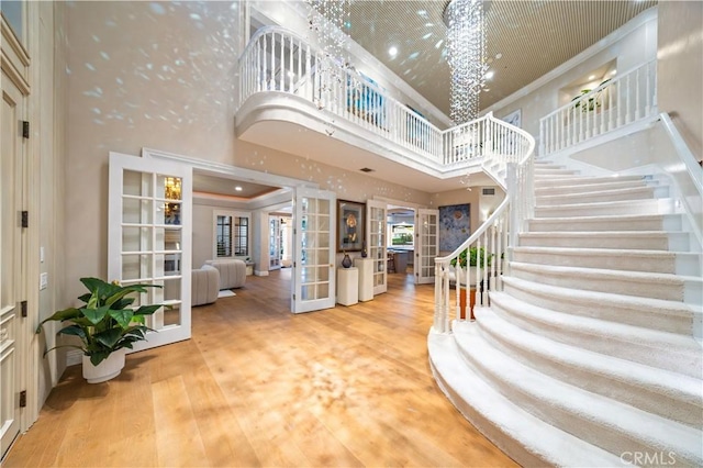 entrance foyer with a towering ceiling, ornamental molding, wood finished floors, stairs, and french doors