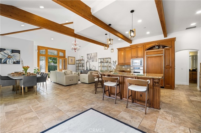 kitchen featuring arched walkways, stone tile floors, stainless steel appliances, a breakfast bar, and brown cabinetry