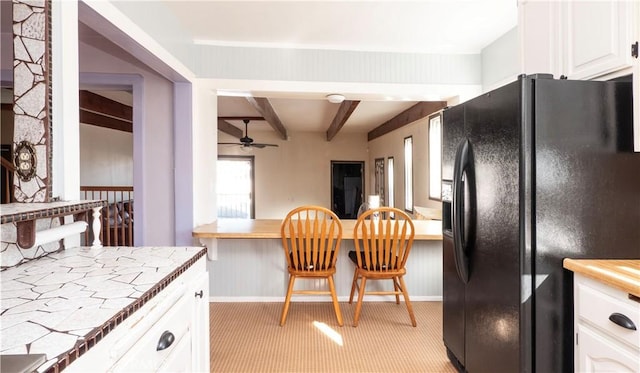 kitchen featuring light carpet, tile counters, white cabinets, beamed ceiling, and black fridge