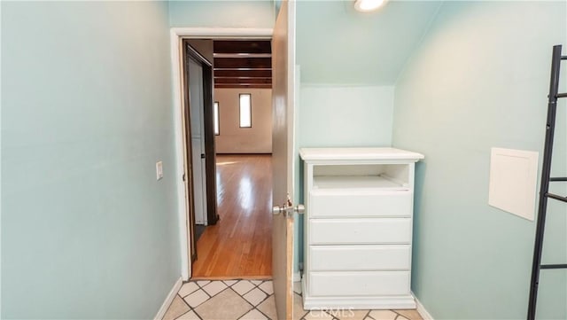 corridor featuring light tile patterned flooring, vaulted ceiling, and baseboards