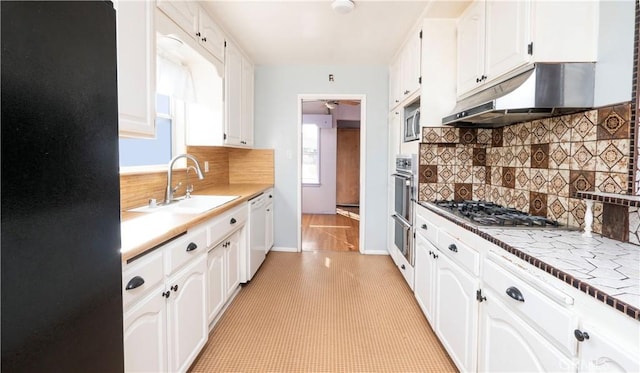 kitchen with under cabinet range hood, stainless steel appliances, a sink, white cabinets, and backsplash