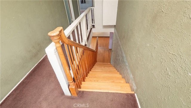 stairway featuring a textured wall, carpet floors, and baseboards