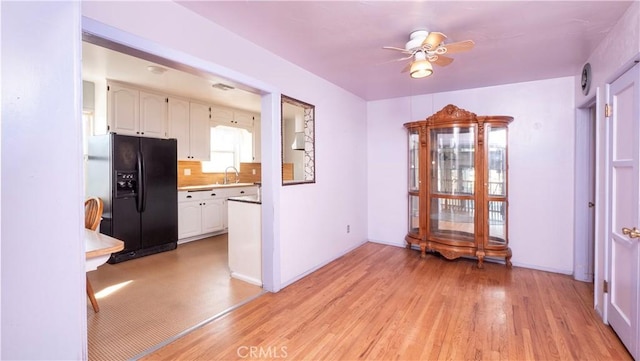 unfurnished dining area with light wood-type flooring, baseboards, a ceiling fan, and a sink