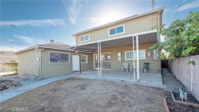 rear view of house with a patio area, fence, and stucco siding