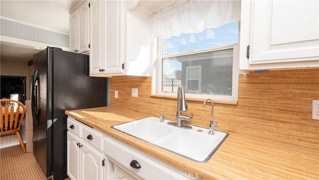 kitchen with backsplash, white cabinets, a sink, and freestanding refrigerator