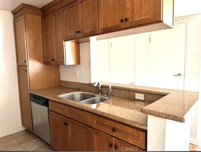 kitchen with light tile patterned floors, dishwasher, light stone counters, brown cabinets, and a sink