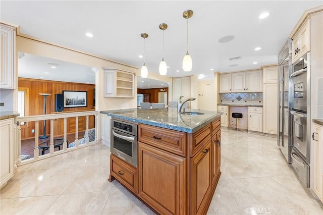 kitchen featuring cream cabinetry, decorative backsplash, double oven, a sink, and dark stone countertops