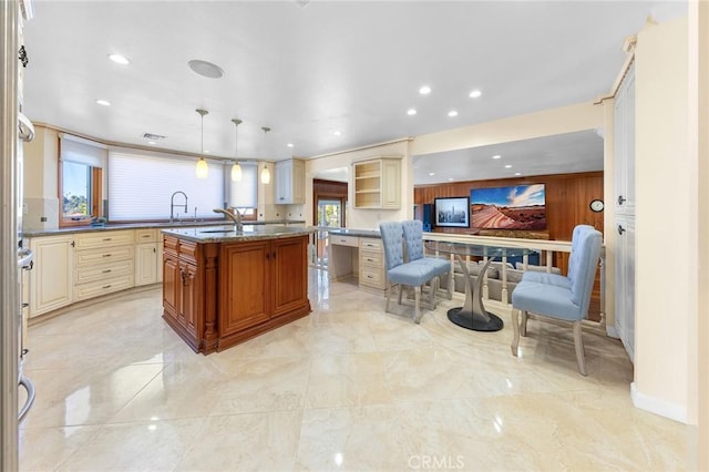 kitchen with a sink, plenty of natural light, cream cabinets, and dark stone countertops