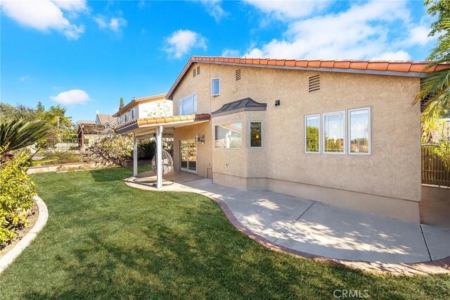 rear view of house featuring a patio, a lawn, fence, and stucco siding