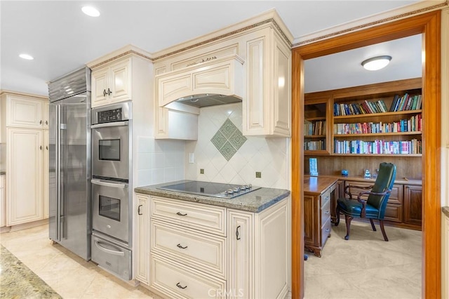 kitchen with light stone counters, cream cabinetry, a warming drawer, built in desk, and stainless steel appliances