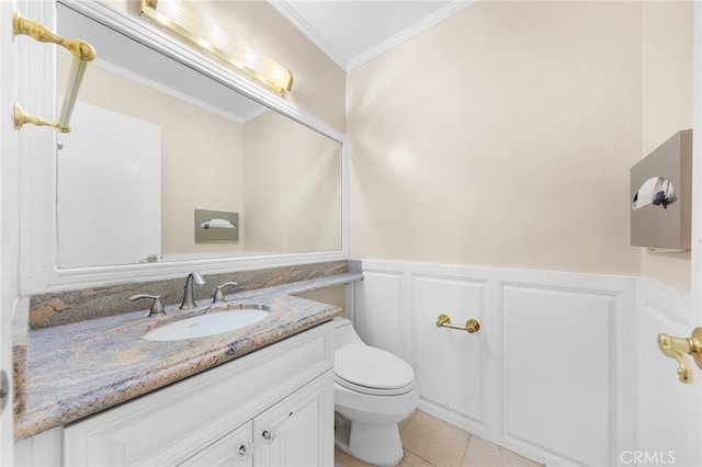 half bath with a wainscoted wall, crown molding, toilet, vanity, and tile patterned flooring