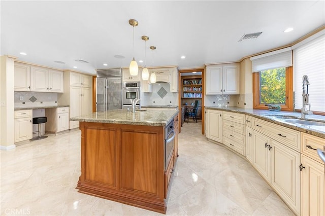 kitchen featuring cream cabinetry, built in desk, visible vents, appliances with stainless steel finishes, and a sink