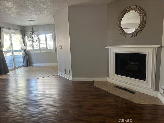 unfurnished living room featuring a textured ceiling, a fireplace with flush hearth, wood finished floors, visible vents, and an inviting chandelier