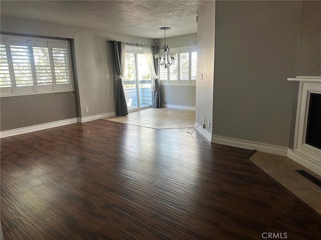 unfurnished dining area featuring a chandelier, a textured ceiling, baseboards, and wood finished floors