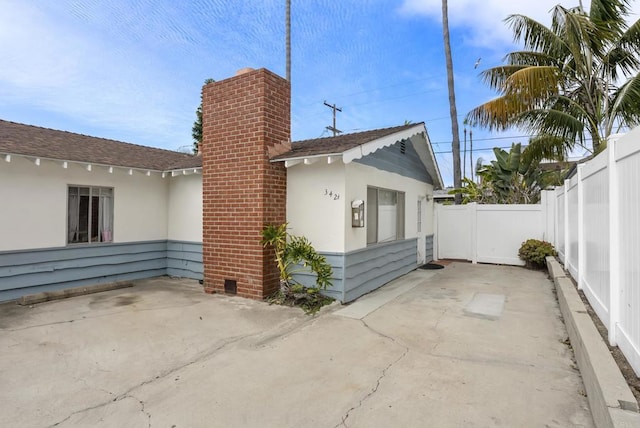 view of property exterior featuring a patio, a chimney, fence, and stucco siding