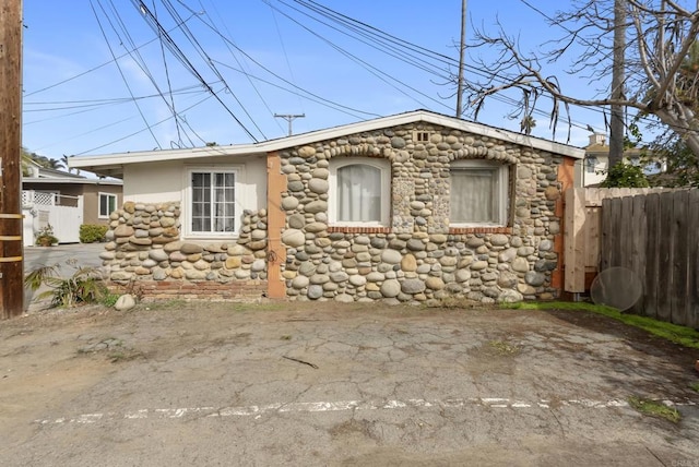 view of side of property with stone siding, fence, and stucco siding