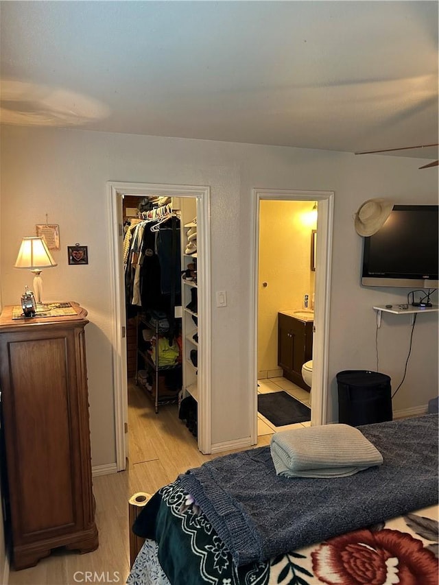 bedroom featuring a walk in closet, a closet, connected bathroom, light wood-style floors, and baseboards