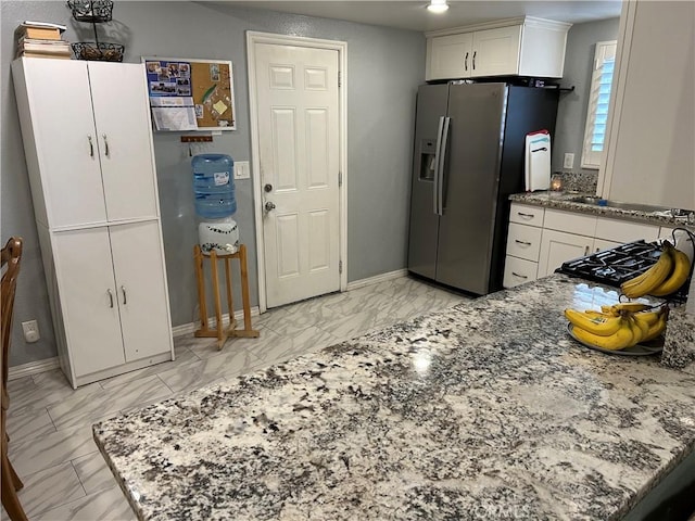 kitchen featuring baseboards, stone counters, stainless steel fridge, marble finish floor, and white cabinetry