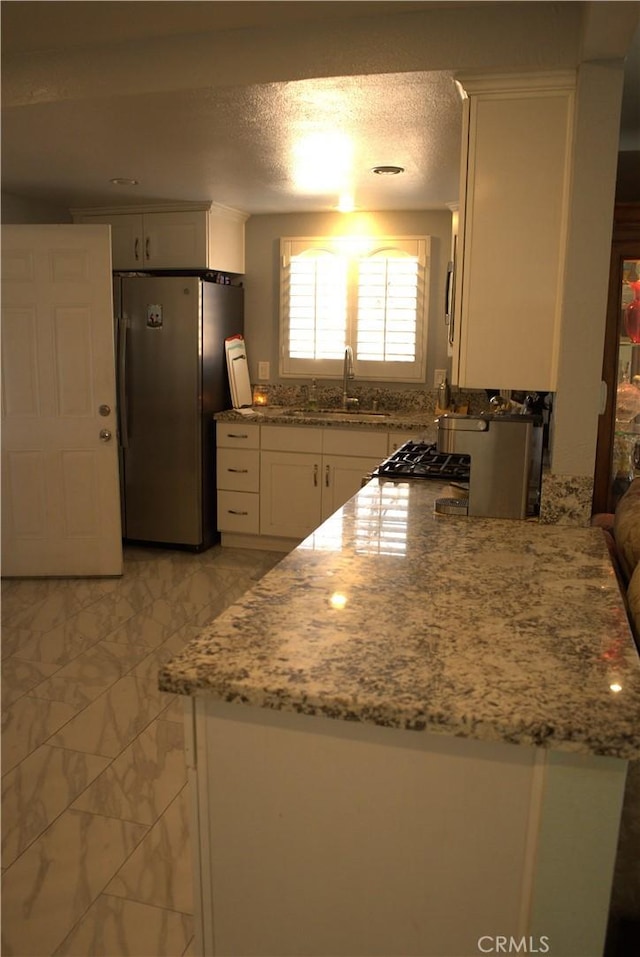 kitchen with light stone countertops, stainless steel appliances, marble finish floor, white cabinetry, and a sink