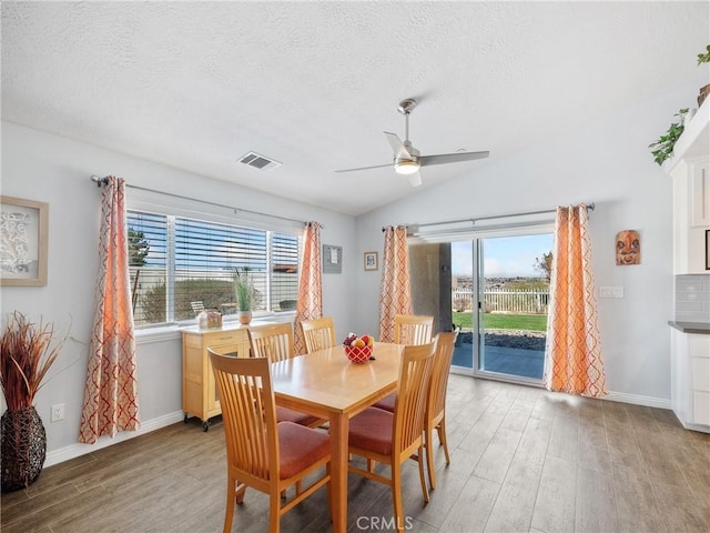 dining room with lofted ceiling, a textured ceiling, light wood-type flooring, and visible vents