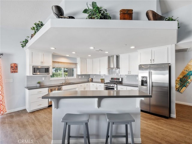 kitchen with light wood-style flooring, stainless steel appliances, a sink, wall chimney range hood, and dark countertops