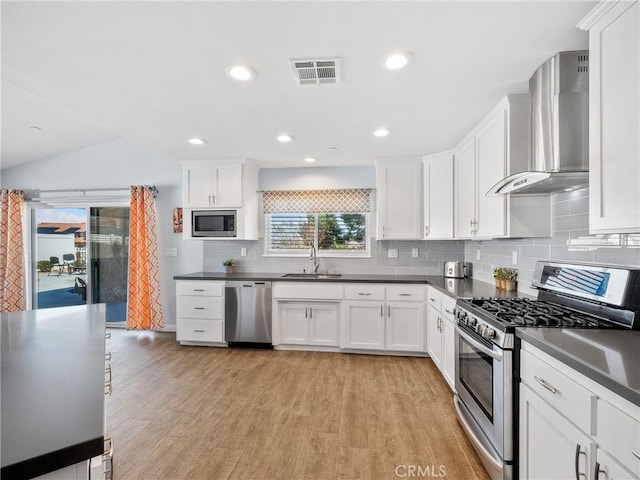 kitchen with visible vents, dark countertops, stainless steel appliances, wall chimney range hood, and a sink