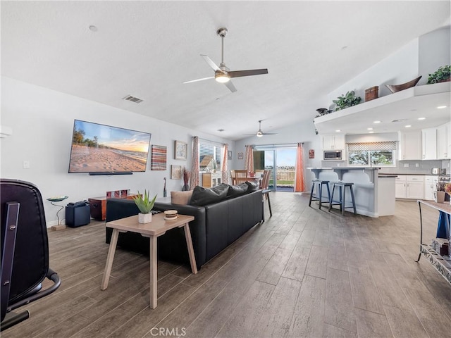 living room with light wood-type flooring, lofted ceiling, visible vents, and a ceiling fan