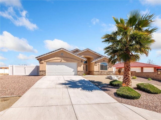 mediterranean / spanish-style home with a garage, stone siding, fence, and stucco siding