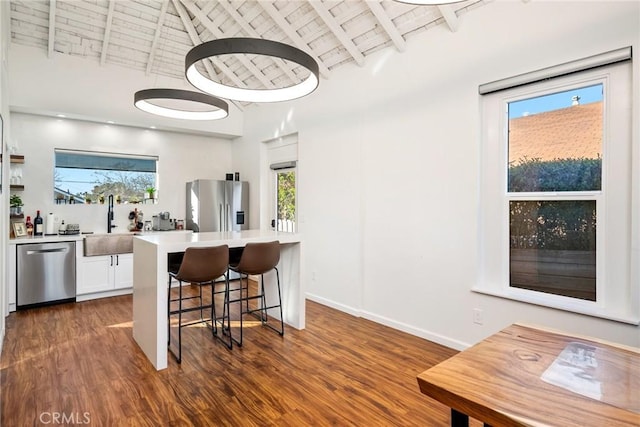 kitchen featuring dark wood-style floors, a breakfast bar area, stainless steel appliances, a sink, and wooden ceiling