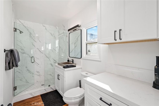 bathroom featuring toilet, a marble finish shower, and vanity